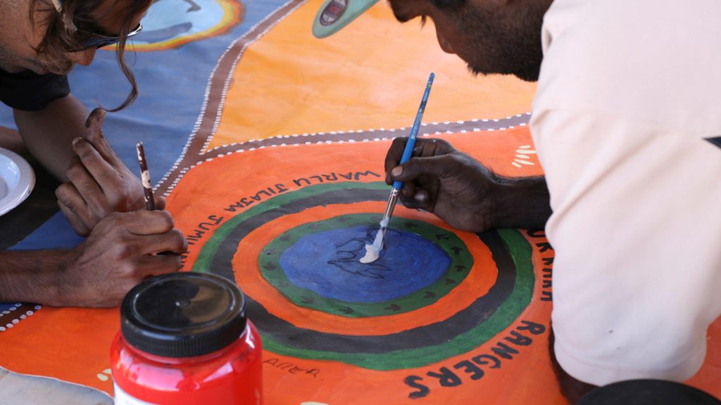 A picture of Ngurrara Rangers painting on canvas in rich desert colours.